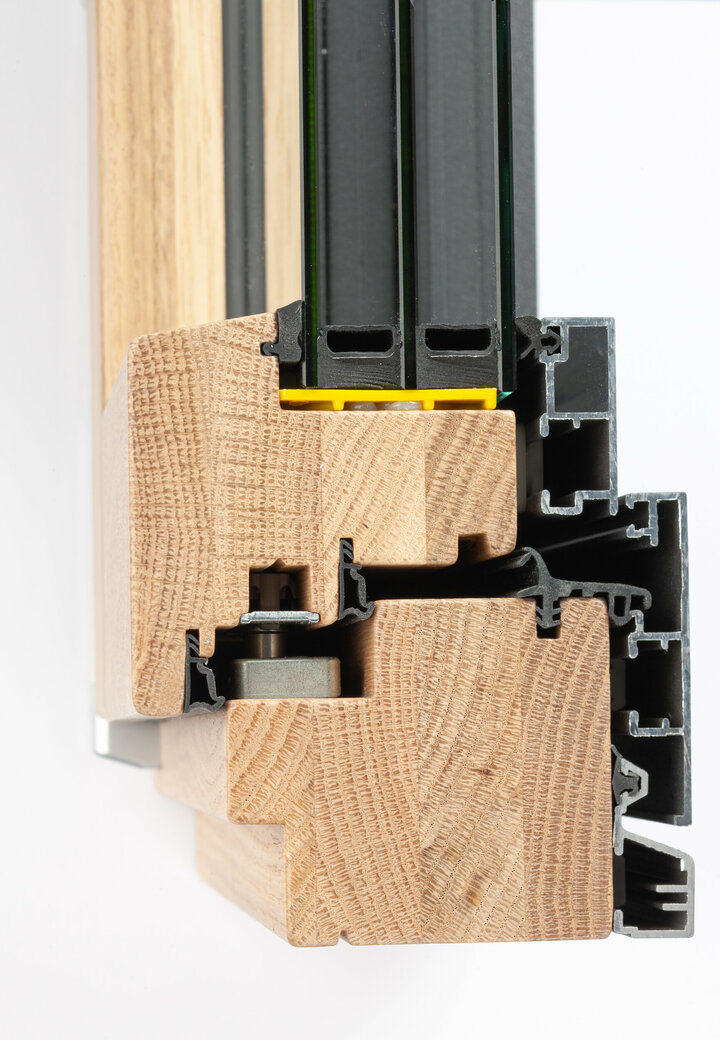 Der Querschnitt eines Fensters zeigt einen Holzrahmen mit einem schwarzen Metallrahmen vor einem weißen Hintergrund.