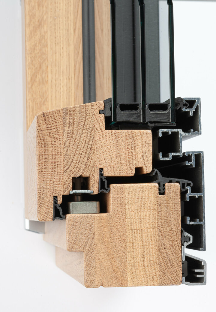 Ein Querschnitt durch einen hölzernen Fensterrahmen zeigt eine helle Holzmaserung, einen schwarzen Metallrahmen.