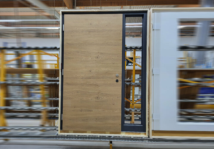 Eine Holztür mit festem Glasseitenteil steht auf einem Transportband in einer Lagerhalle. Das besondere an der Tür ist das Eiche-Türblatt.