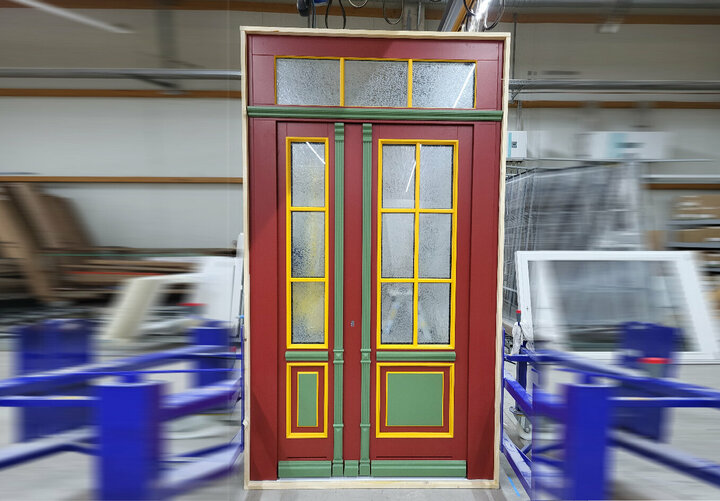 Eine rote Holztür mit Oberlicht und Ornamentgläsern steht in der Produktionshalle und wird für den Versand vorbereitet.