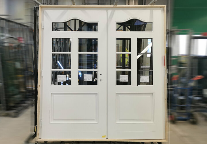 Eine weiße Doppeltür mit sechs Glasscheiben und einem schwarzen Griff steht in einer geschäftigen Werkstatt, umgeben von Werkzeugen und Geräten.