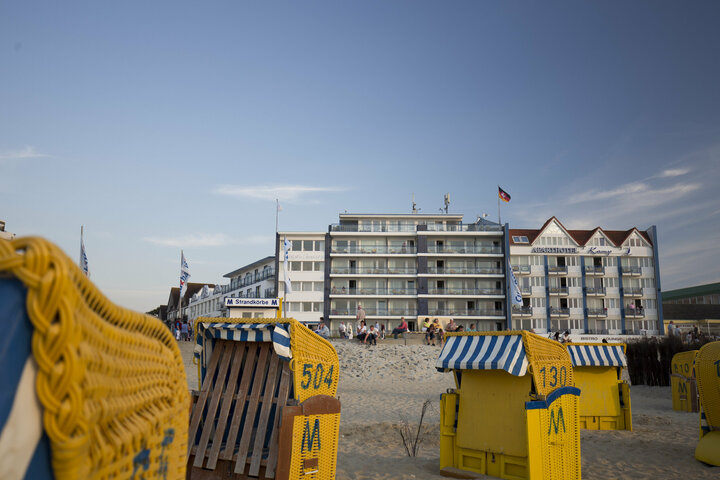 Im Hintergrund ist ein Hotel am Strand zu sehen, begleitet von Strandkörben.