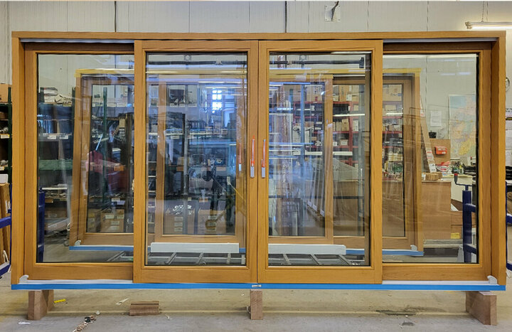 Eine große hölzerne Schiebetür mit zwei Gangflügeln und silbernen Griffen ist in einer Werkstatt ausgestellt, umgeben von Werkzeugen und Geräten.