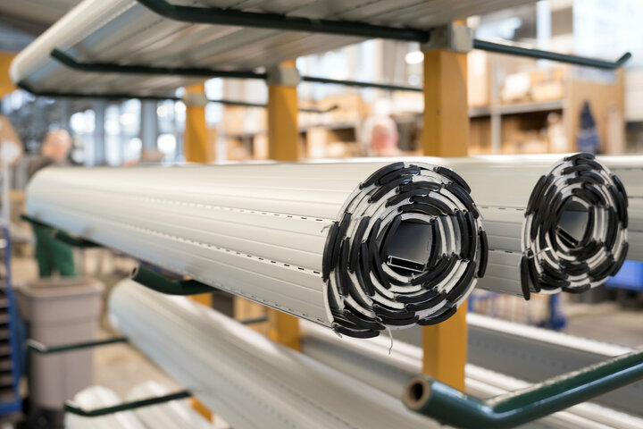 Zwei Rollen Rollladenpanzer sind auf einem grünen Metallgestell in einem Lagerhaus ausgestellt, mit einem unscharfen Hintergrund aus Regalen und Kisten.