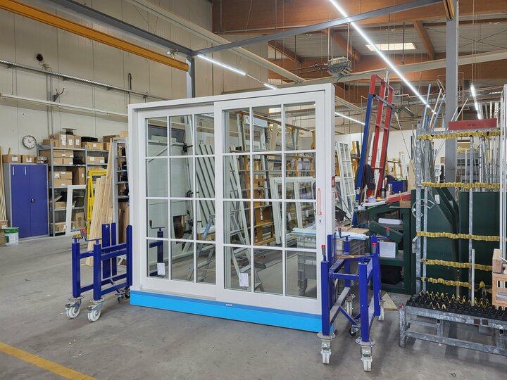 Eine weiße Schiebetür steht in einem belebten Lagerhaus, umgeben von verschiedenen Werkzeugen und Materialien.