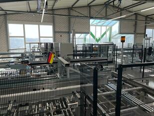 Ein modernes Fabrikinterieur mit einem großen Fenster, Metallträgern und einer gelben Flagge, mit einem schwarzen Metallzaun und einer rot-weiß gestreiften Flagge im Vordergrund.